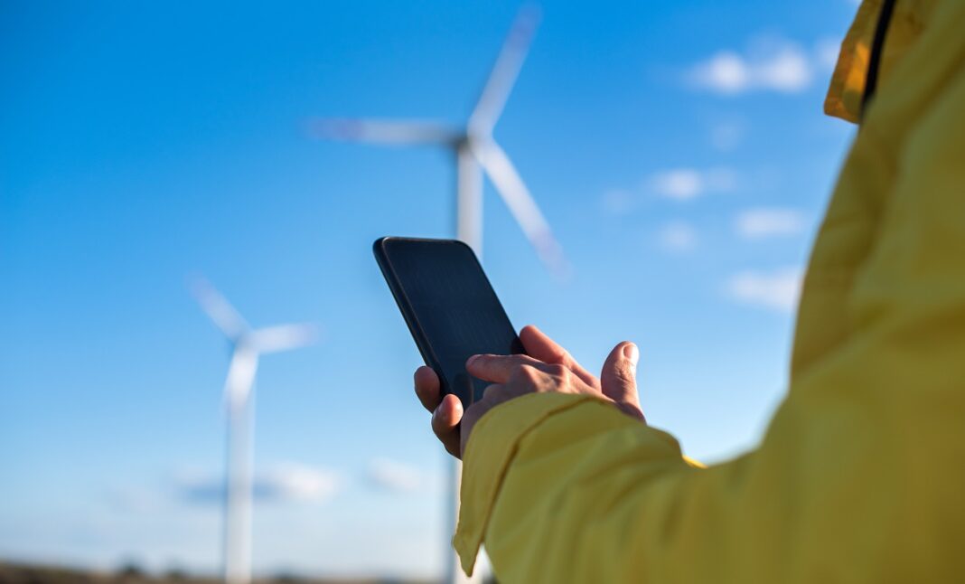 The specialist in yellow uses a gadget to control the parameters of wind turbines. Energie Rinnovabili Telco Mobile Gsma -The specialist uses a gadget to control the parameters of wind turbines. (licenza: Magnific)
